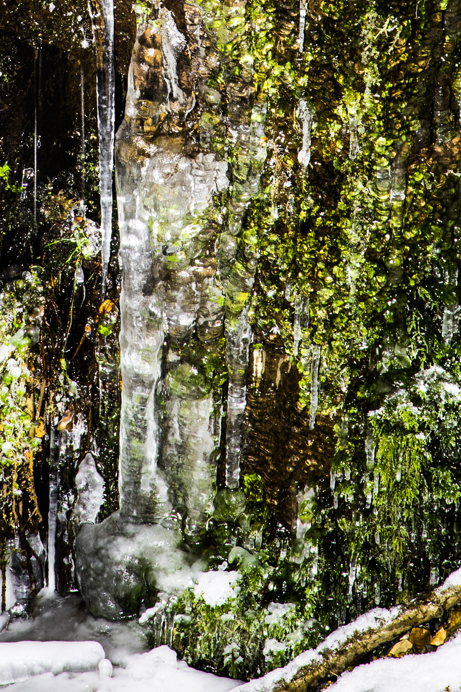Detailaufnahme des mit Moos und Eiszapfen bedeckten Sandsteinsockels am Wasserzulauf
